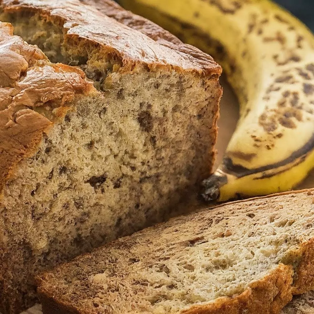 A golden-brown loaf of homemade banana bread with slices on a wooden board, garnished with banana slices.