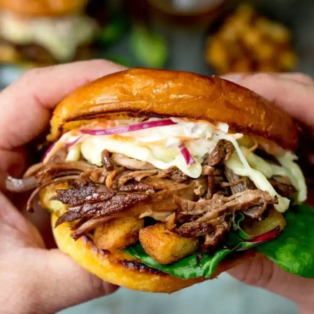 A delicious beef brisket sandwich on a plate, featuring tender slices of brisket layered with fresh vegetables and sauce.
