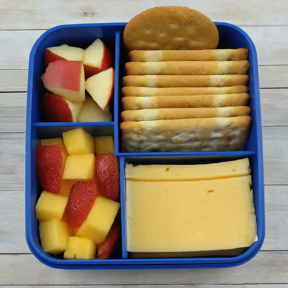 A colorful and neatly arranged lunchbox filled with assorted cheeses, crackers, fruits, and nuts.