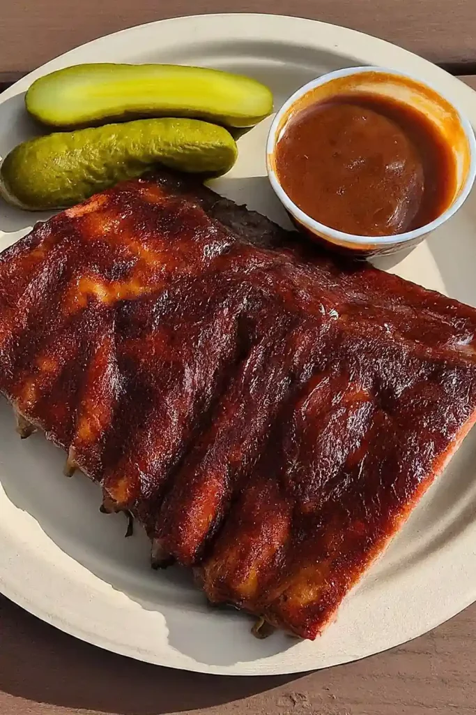 Juicy and tender Traeger-smoked baby back ribs on a wooden cutting board, glazed with BBQ sauce.