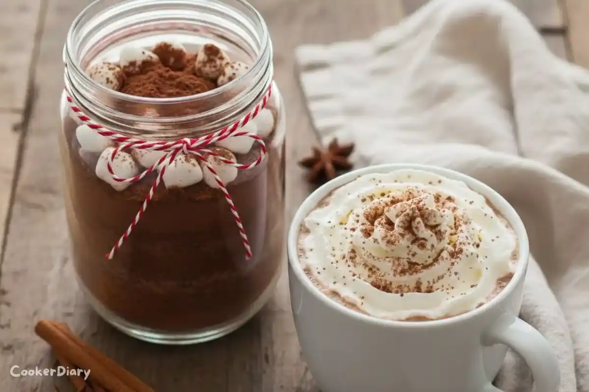 Top-down view of Christmas hot cocoa mix in a glass jar with a mug of hot cocoa.