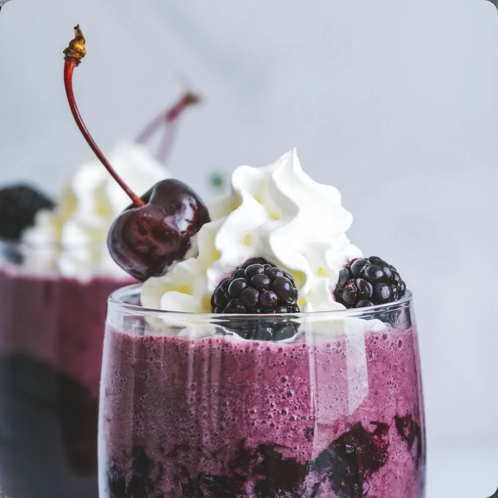 A refreshing glass of black cherry and blackberry smoothie with vibrant colors, garnished with fresh berries on top.