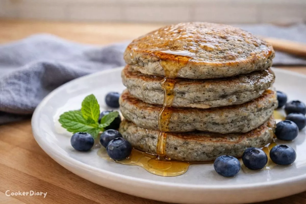 Angled close-up of stacked blue corn pancakes with syrup dripping and blueberries around.