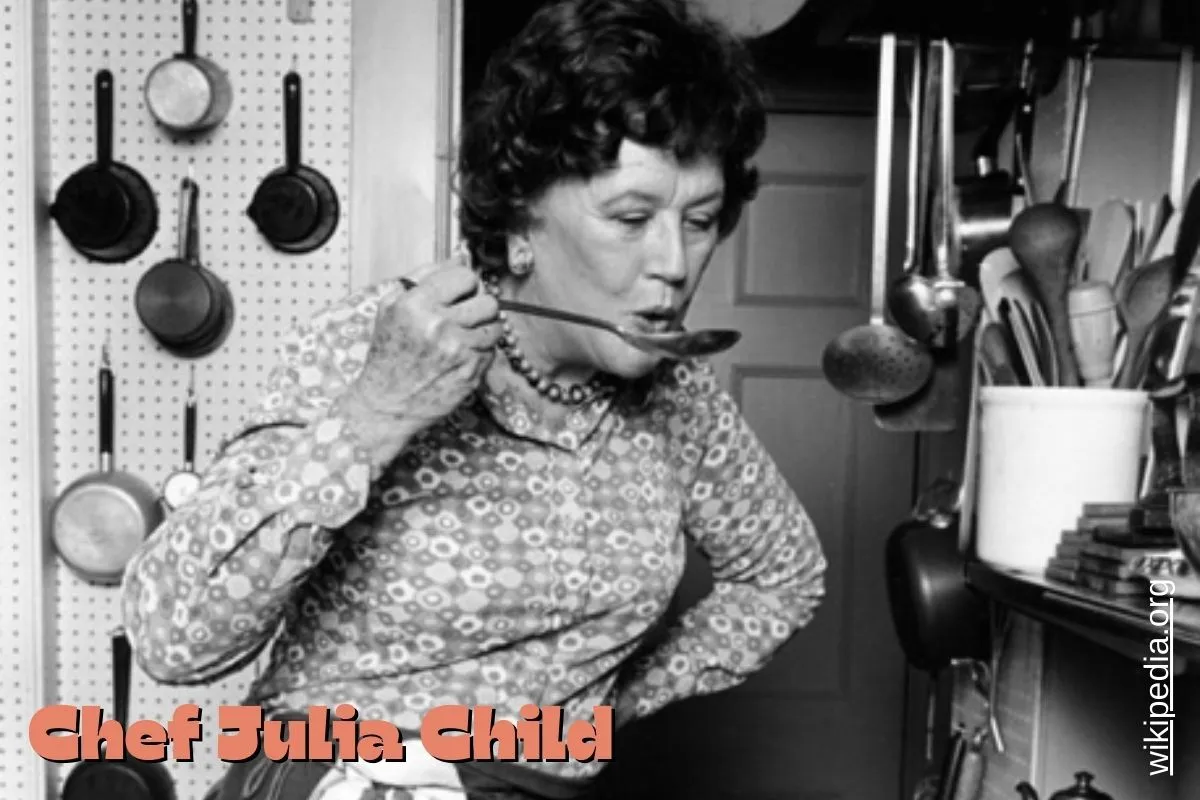1978 publicity portrait of Julia Child standing in her kitchen, smiling warmly while surrounded by cooking utensils and ingredients.