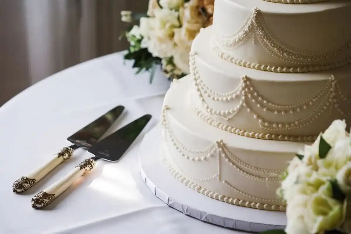 Close-up of a wedding cake being sliced with an elegant cake knife and server set.