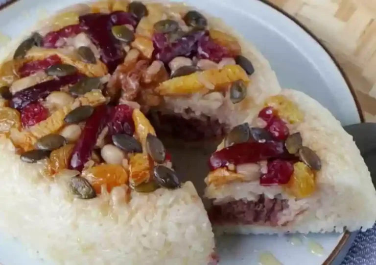 A colorful and layered Ba Bao Fan (Eight Treasure Rice Pudding) dessert, garnished with red bean paste, dried fruits, and nuts.