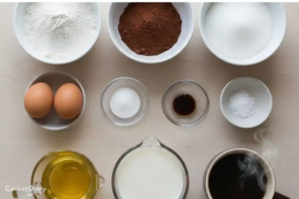 Flat-lay of classic chocolate cake ingredients on a wooden countertop.