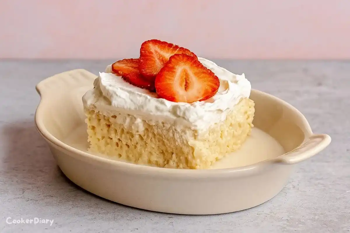 Slice of strawberry tres leches cake topped with fresh strawberries and whipped cream on a dessert plate