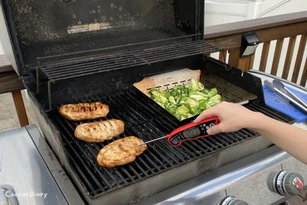 Alpha Grillers digital meat thermometer with metal probe inserted into a steak showing temperature on LCD screen