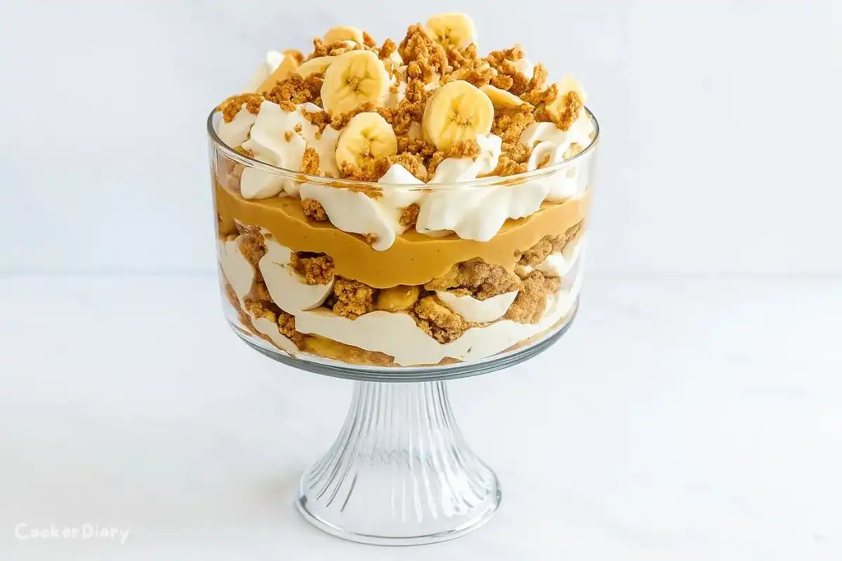Layered banana trifle with peanut butter, whipped cream, and chocolate drizzle in a glass serving bowl