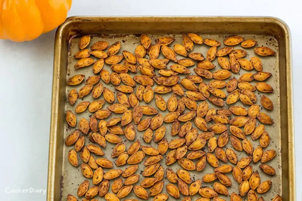 Just baked pumpkin seeds spread out on a baking dish, golden and crispy