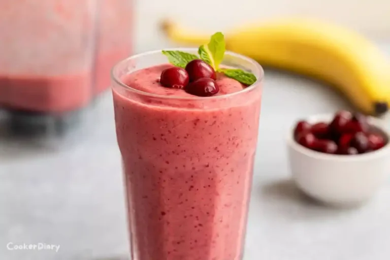Side view of cranberry smoothie in a tall glass with cranberries and mint garnish.