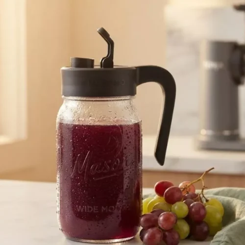 Fresh cold pressed grape juice in a glass jar surrounded by grapes on a marble countertop